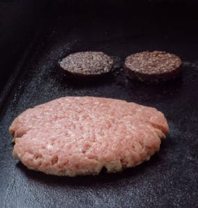 Pork burger and black pudding cooking on a flat top