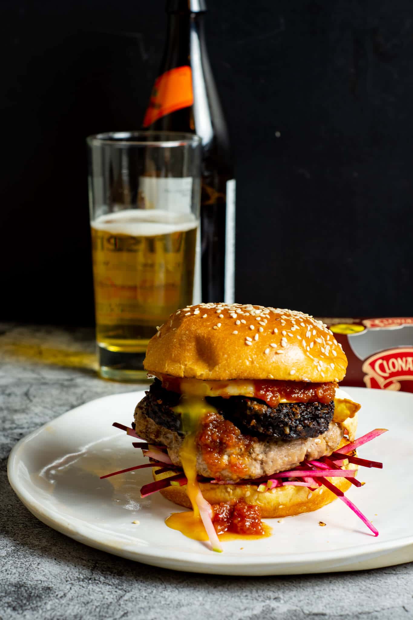Pork & black pudding burger on a white plate with a beer in background