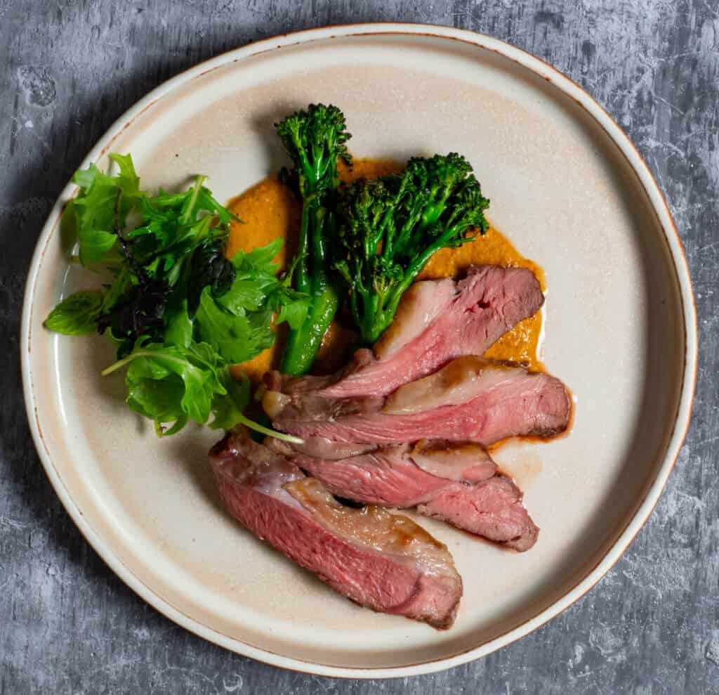 BBQ lamb, romesco sauce & charred broccolini on a plate