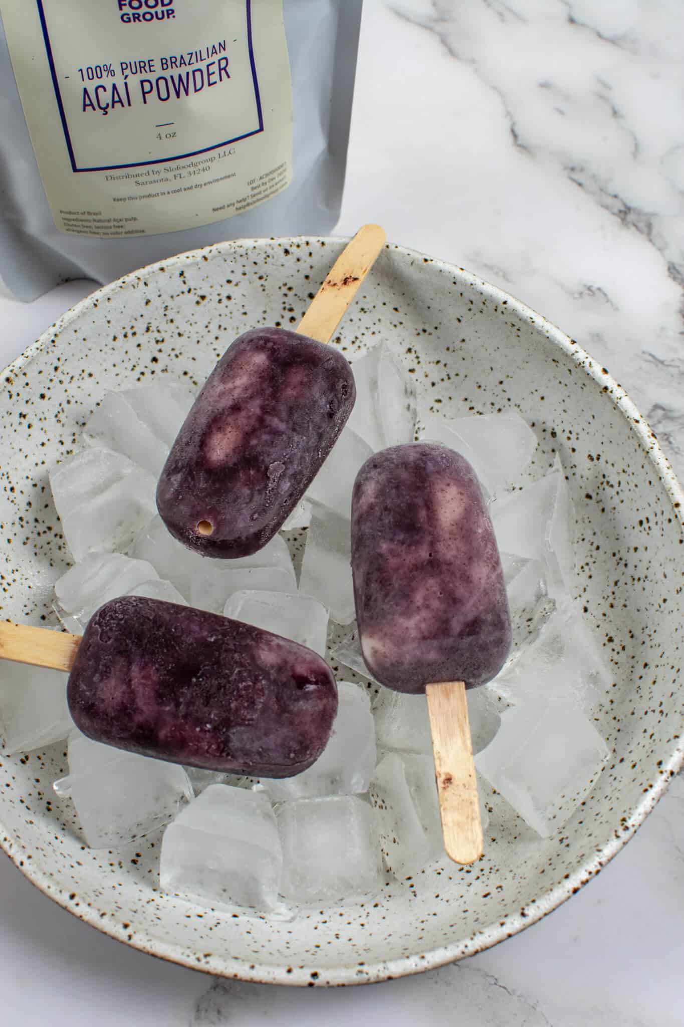 3 acai ice pops in a bowl of ice with packet of slofoodgrp acai