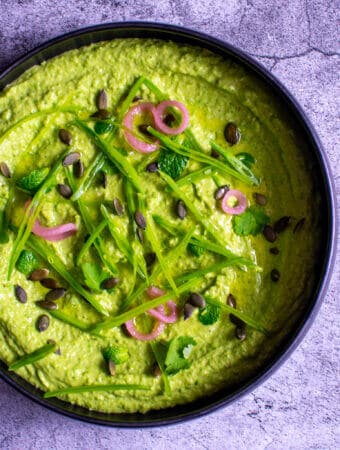 black bowl with avocado & pea hummus topped with pickled onions, pepitas, herbs & snowpeas