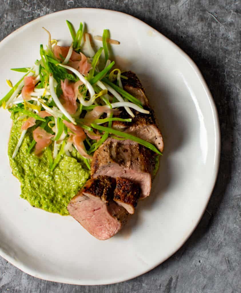 pork loin, avocado & pea hummus & beansprout salad on a plate