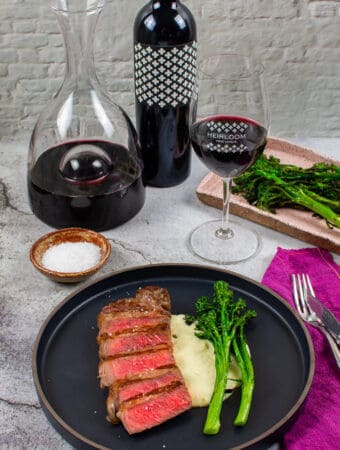 steak & onion soubise on a plate, decanter, glass of wine and bottle heirloom shiraz