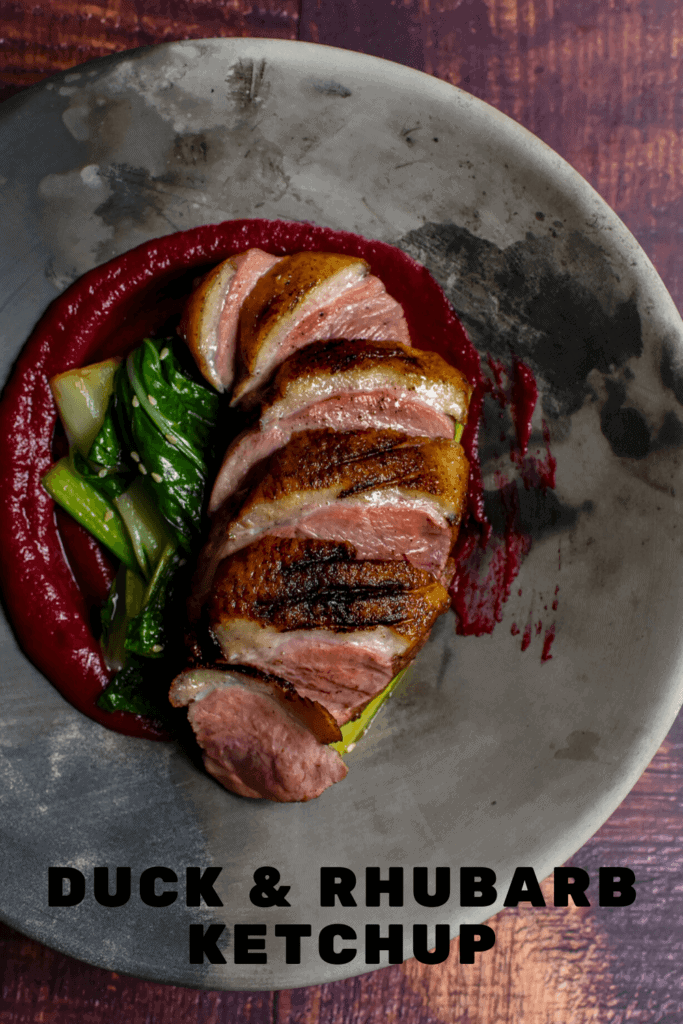 Duck breast, rhubarb ketchup & asian greens in a made of australia bowl on a table