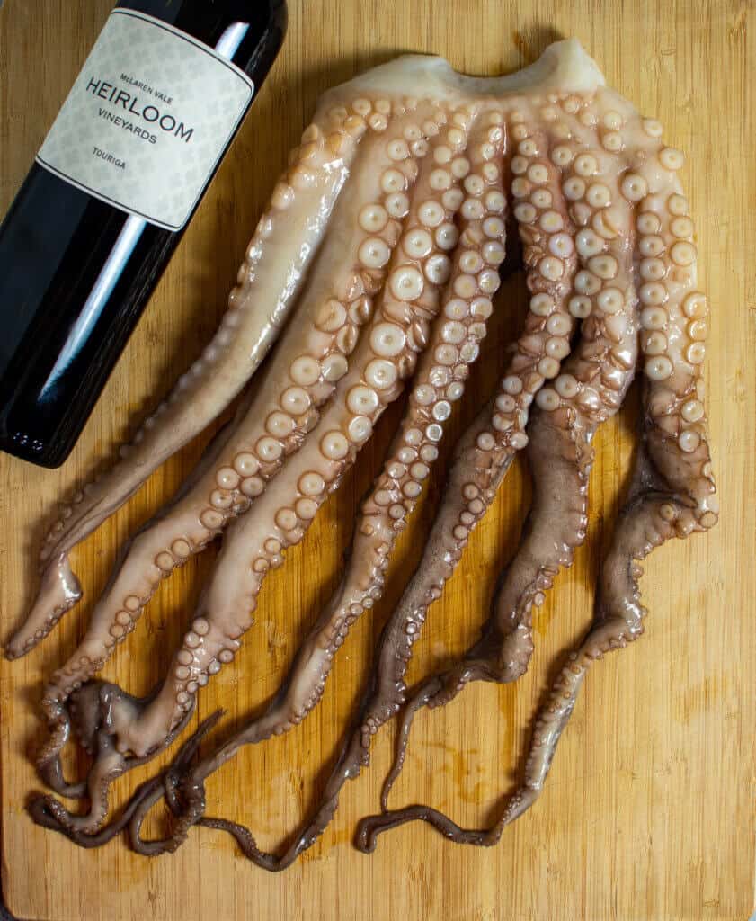 raw octopus on a chopping board with bottle of heirloom red wine