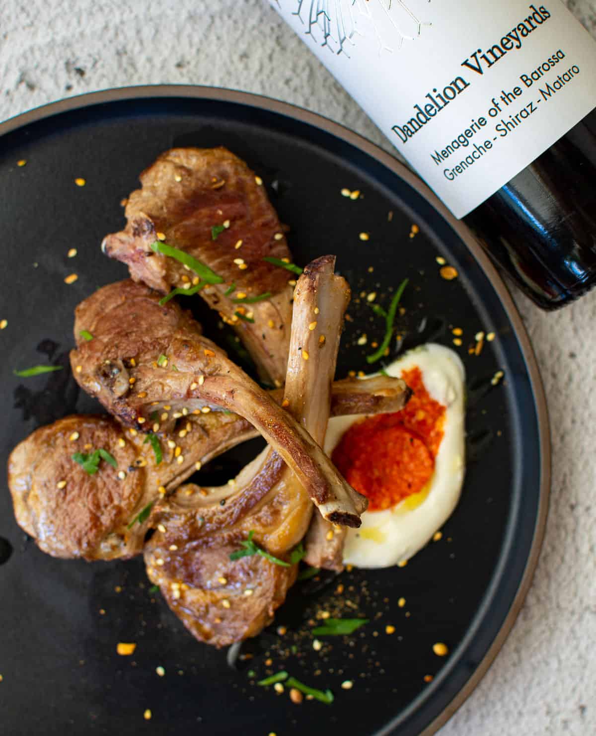 grilled lamb chops on a plate wit harissa & labneh