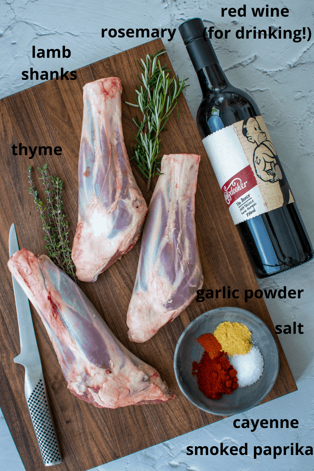 lamb shanks on a chopping board with spices, herbs and a bottle of wine