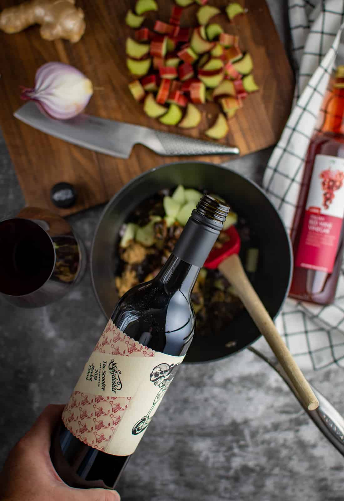 pouring red wine into saucepan with ingredients on a chopping board