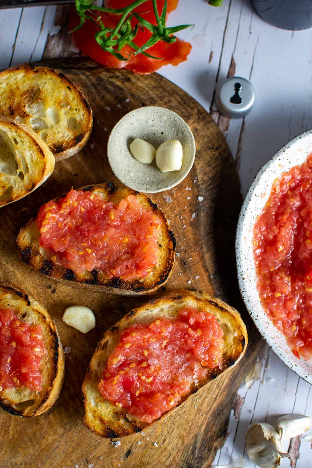 pan con tomate on a wooden board with a bowl of grated tomatoes beside them