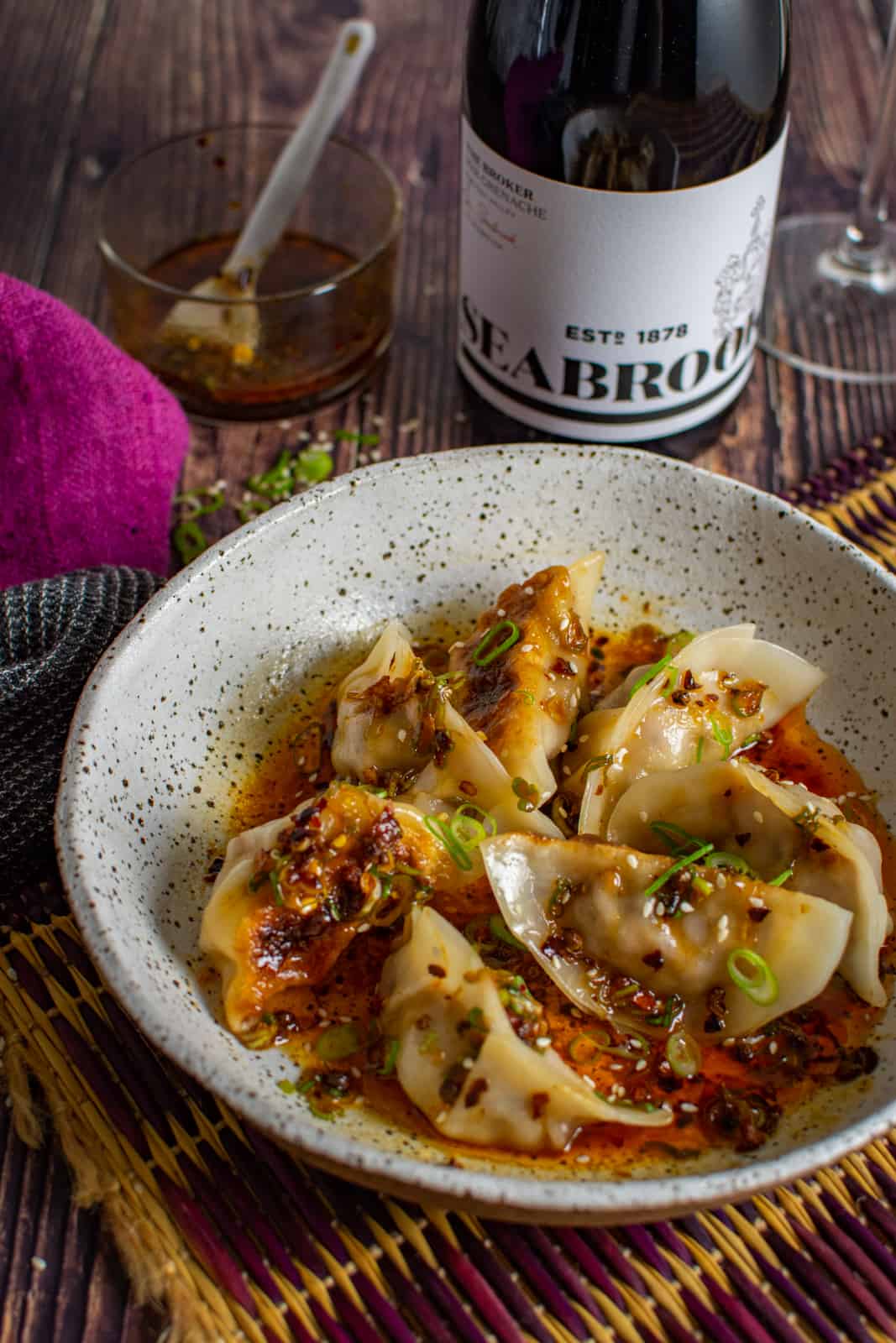 A bowl of pork cabbage dumpling with bottle of red wine behind the bowl 