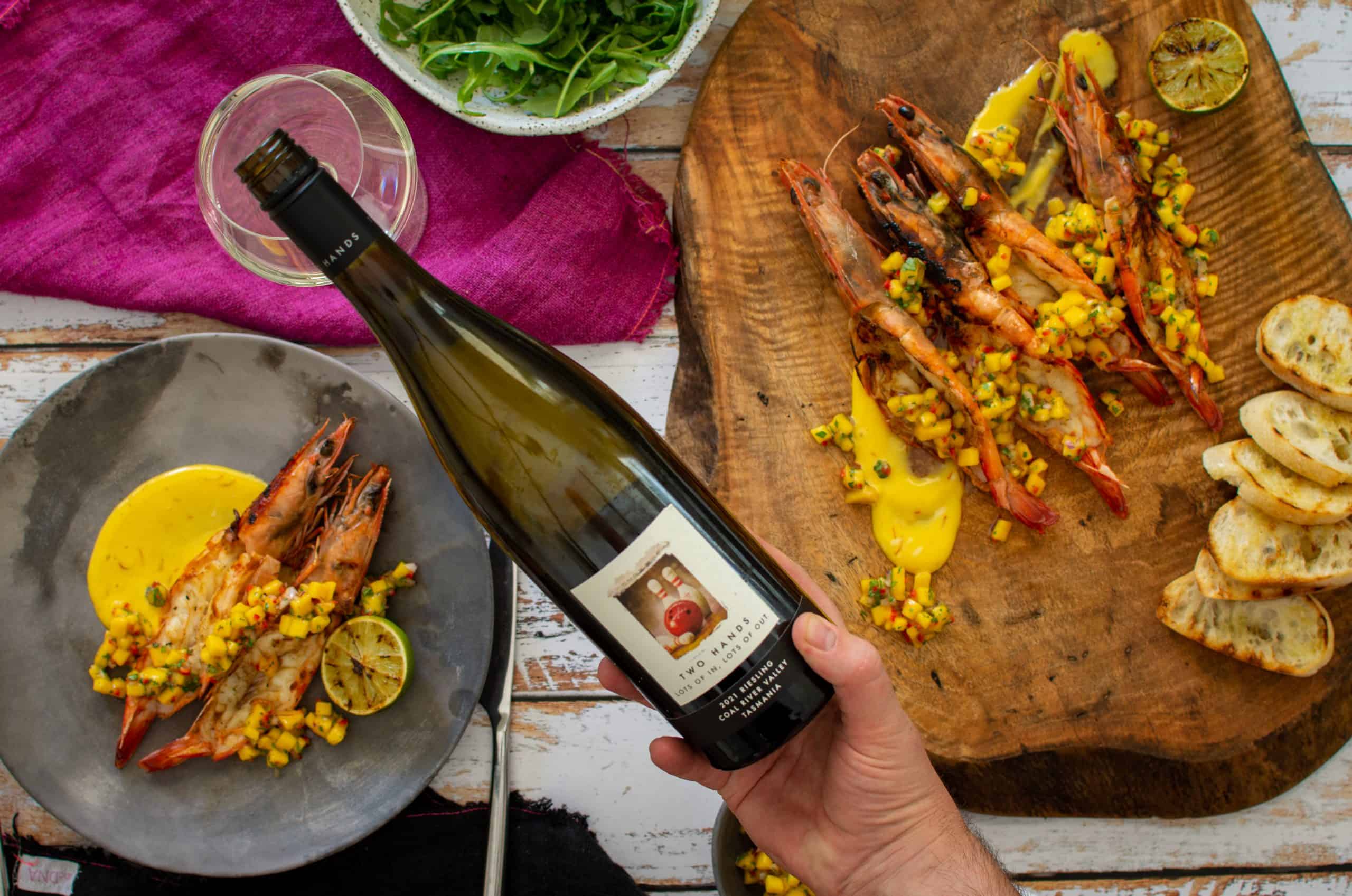 Someone pouring riesling with bbq prawns on a plate/wooden board below 
