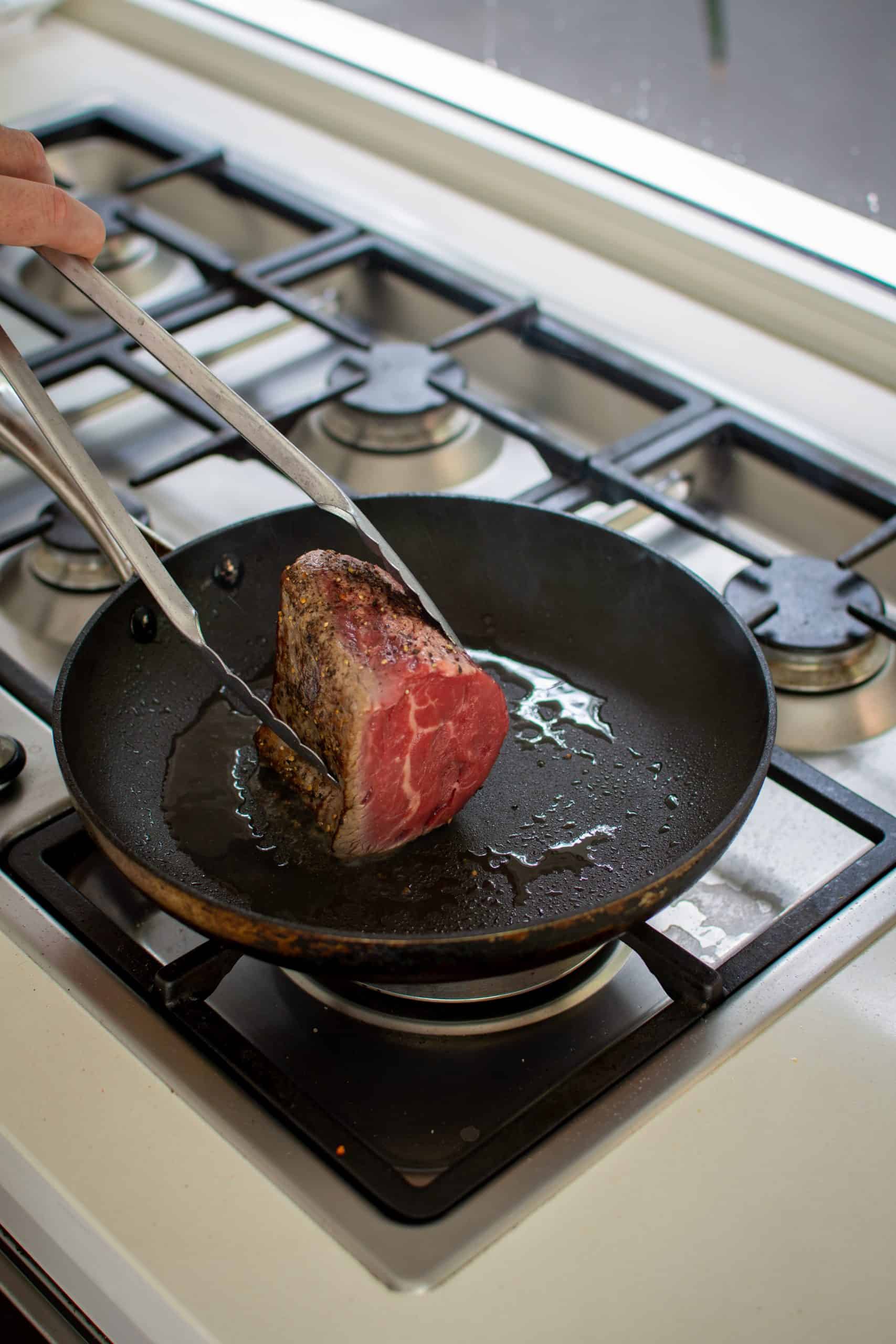 beef tenderloin being seared in frying pan 
