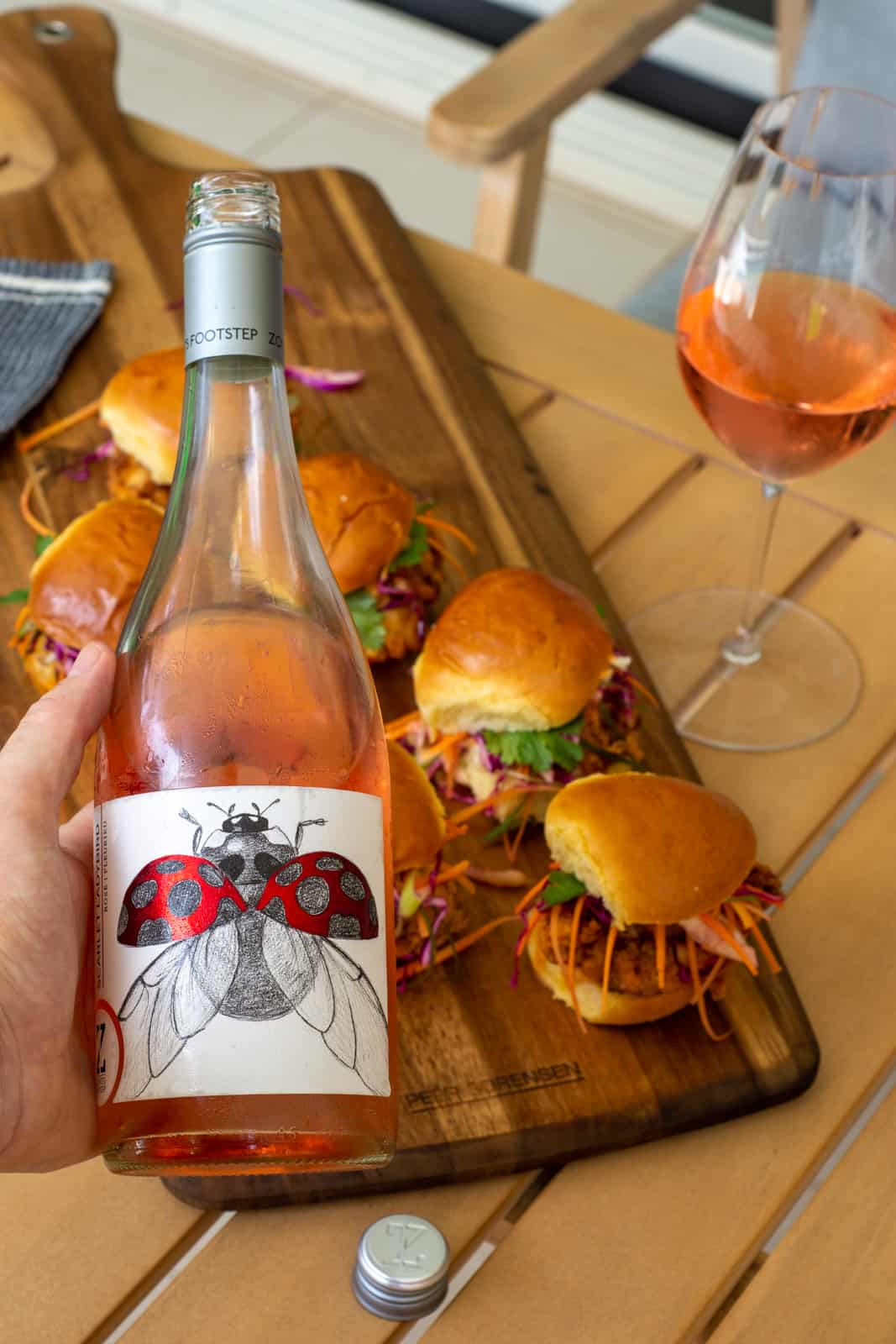 someone holding a bottle of rose wine above a board of fried chicken sliders 