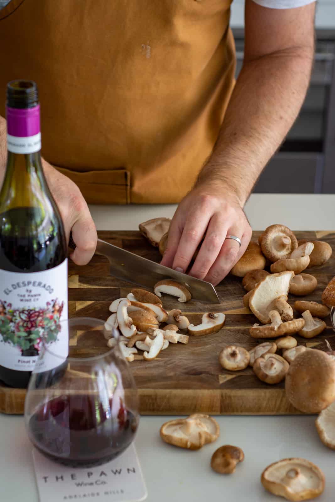 someone chopping shiitake mushrooms in the kicthen with a wine bottle next to them 