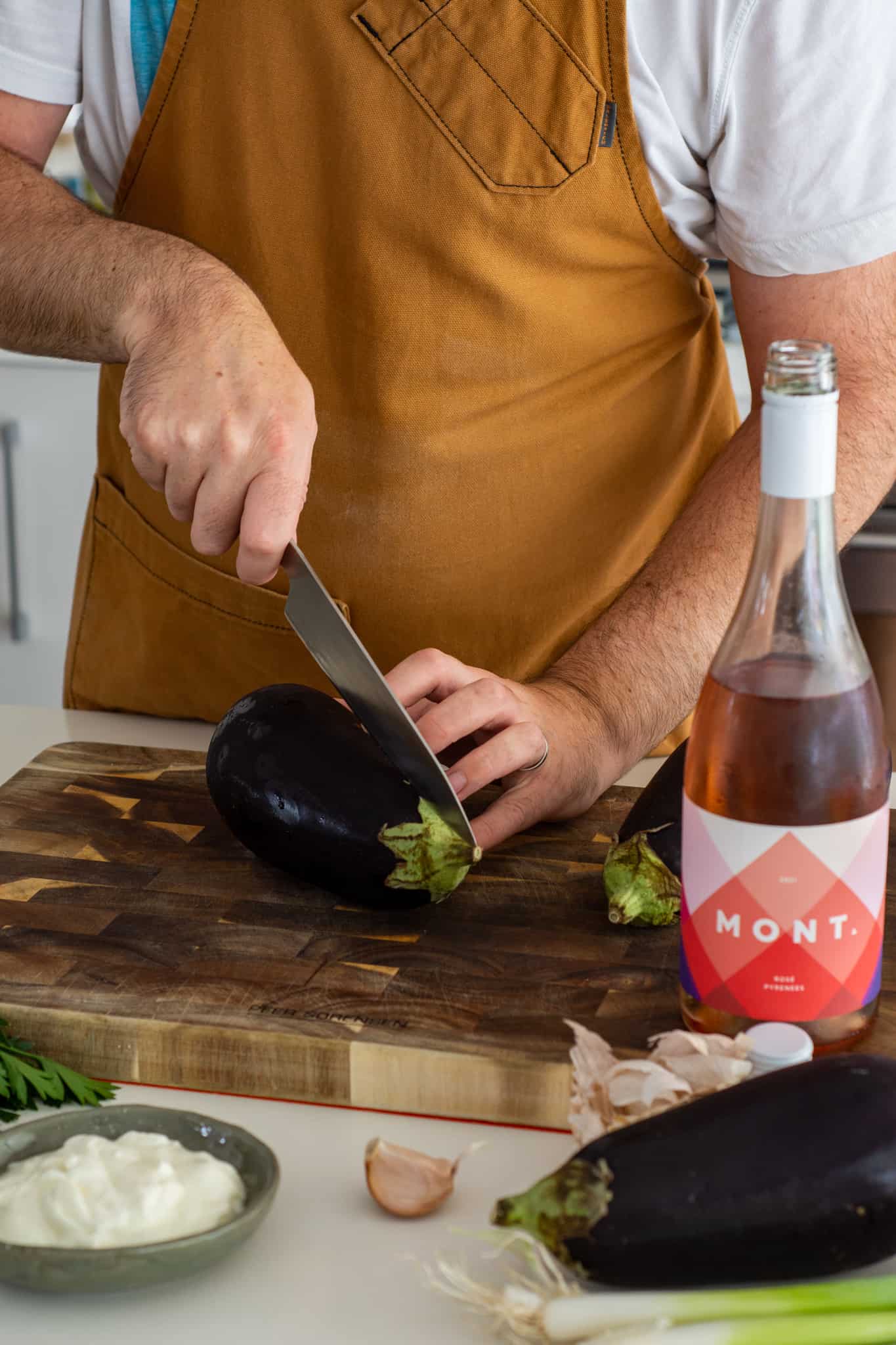 Someone cutting an aubergine on chopping board with rose wine beside them 