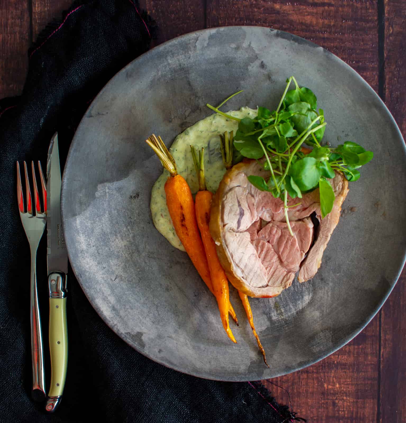 birdseye view of roast lamb on a plate with carrots and chermoula yoghurt