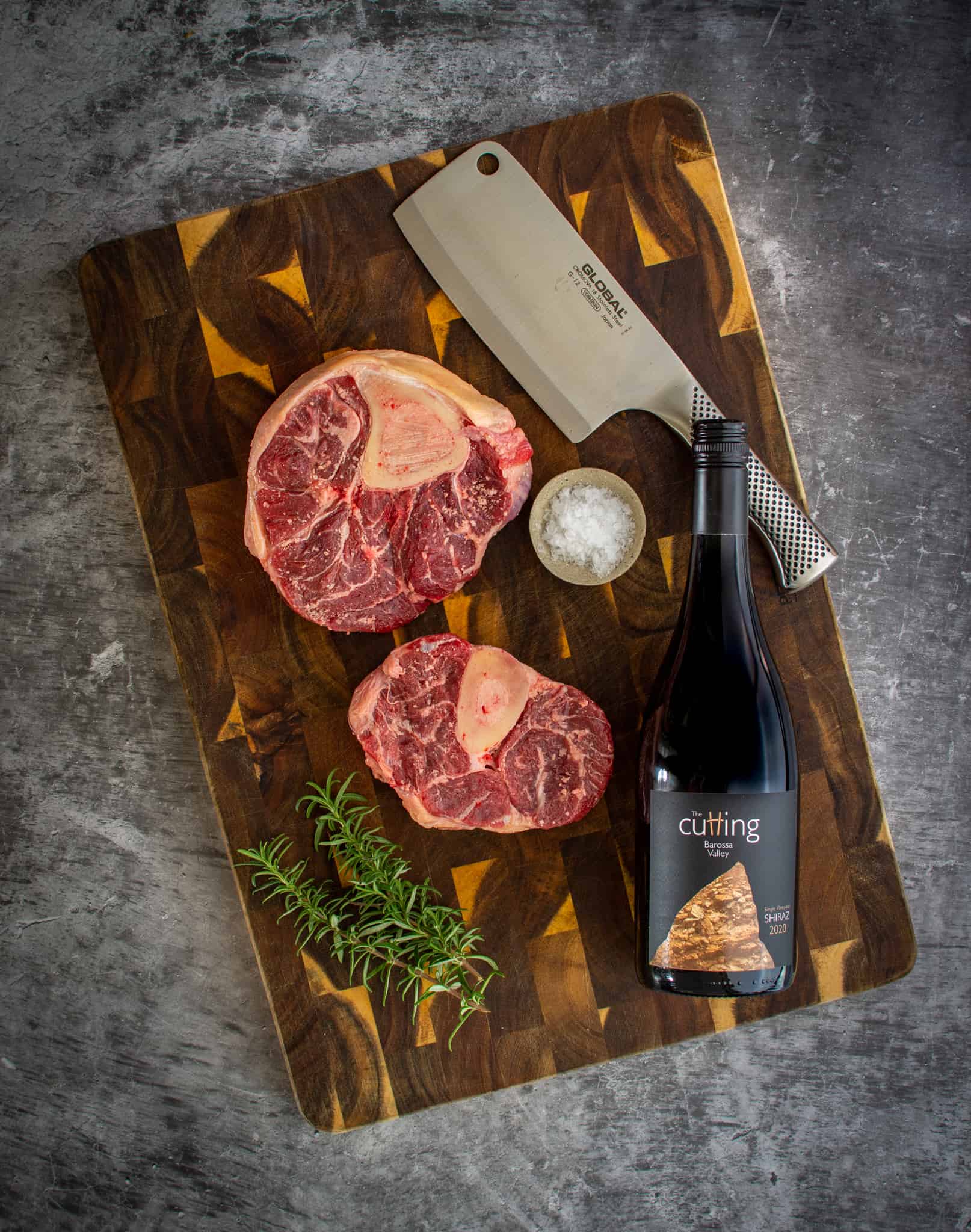 Ossobuco, bottle of red wine and a meat cleaver on a chopping board 