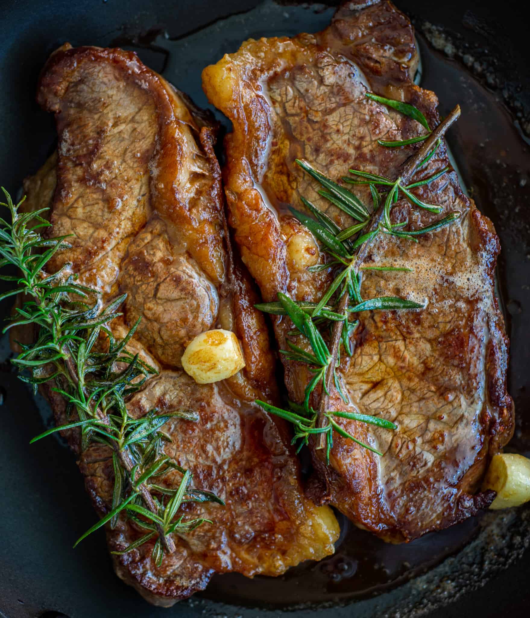 seared striploin steaks in a frying pan with herbs, garlic and butter