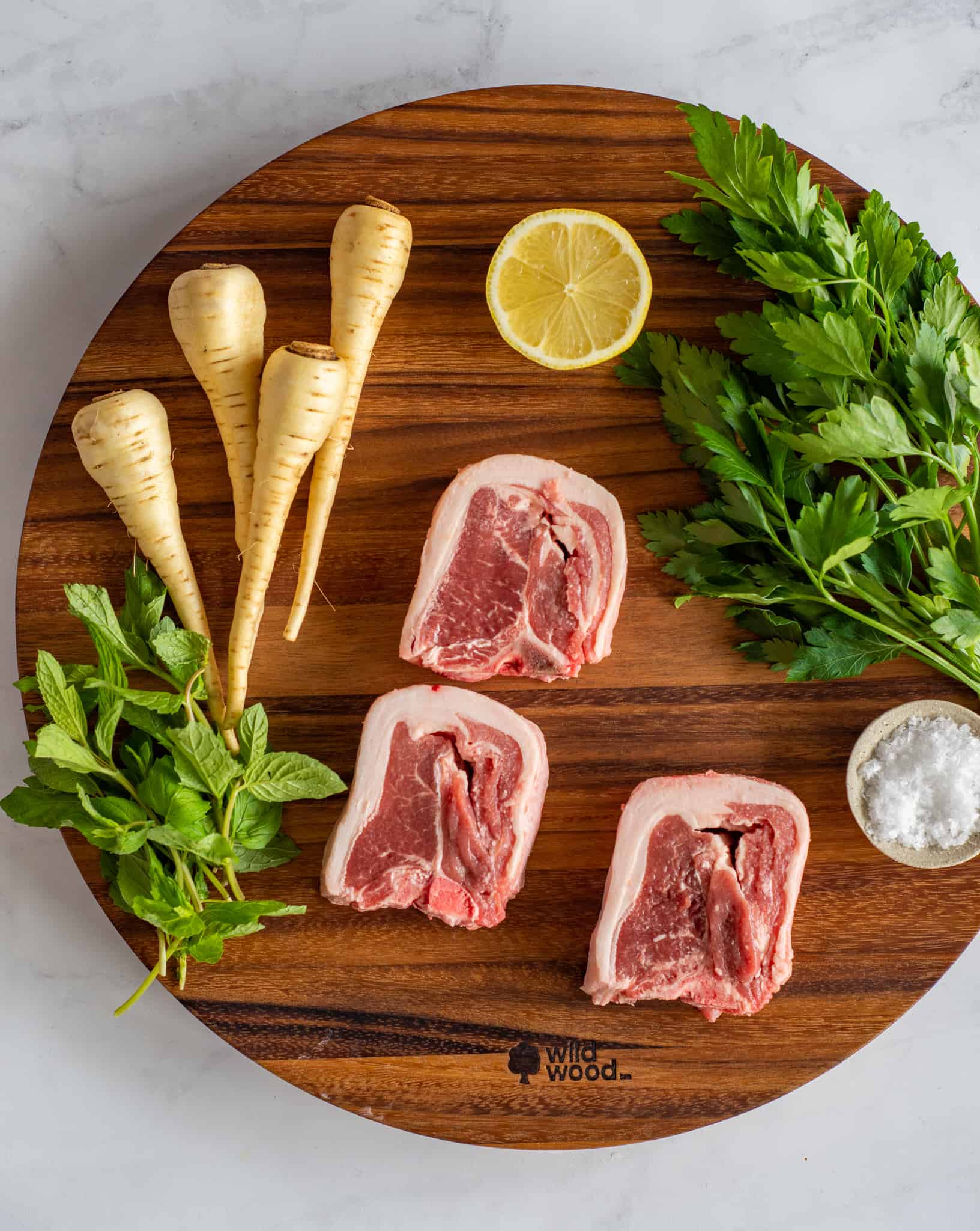 lamb loin chops, parsnips, herbs and salt on a chopping board 