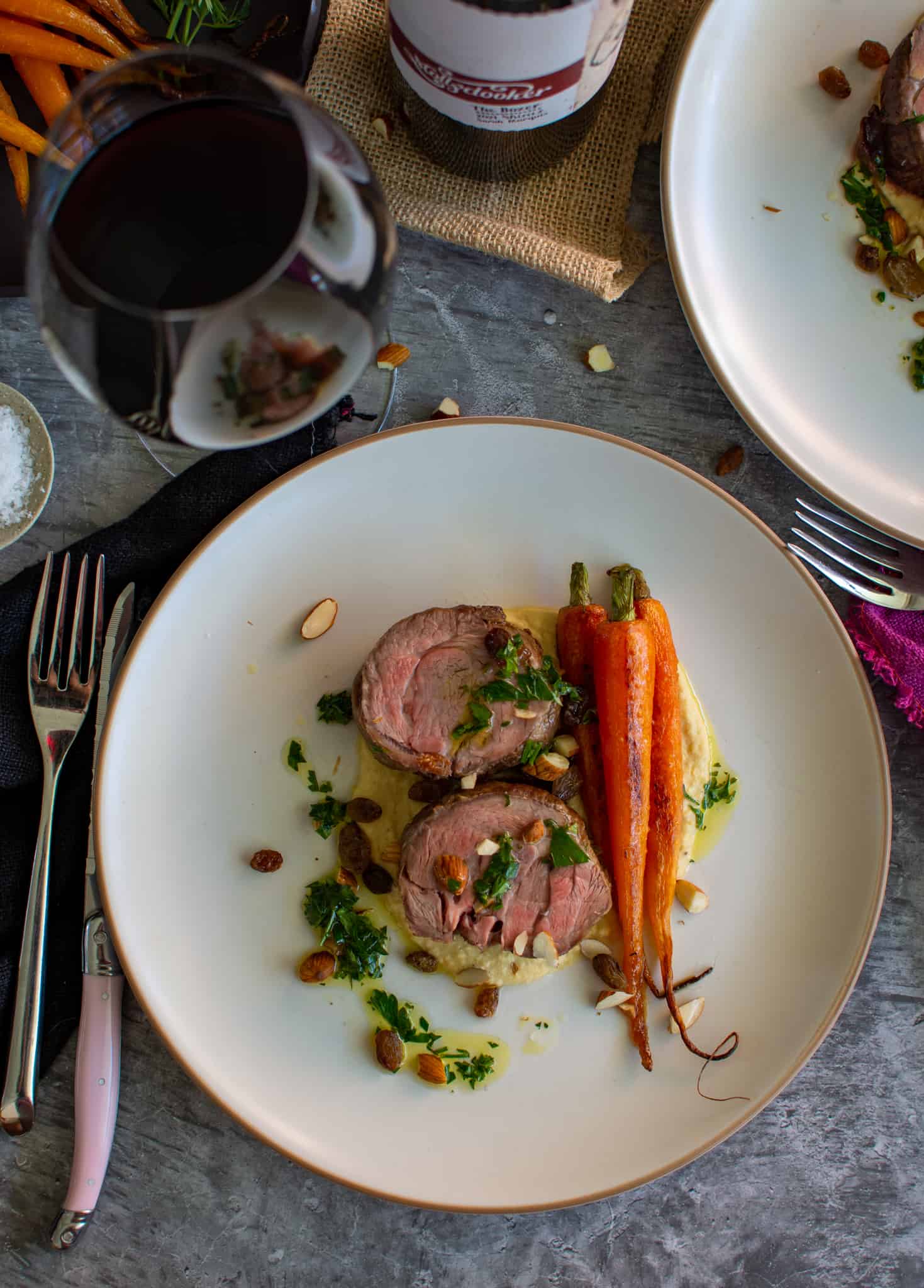 roasted boned lamb shoulder with hummus, carrots and roasted almonds on a plate