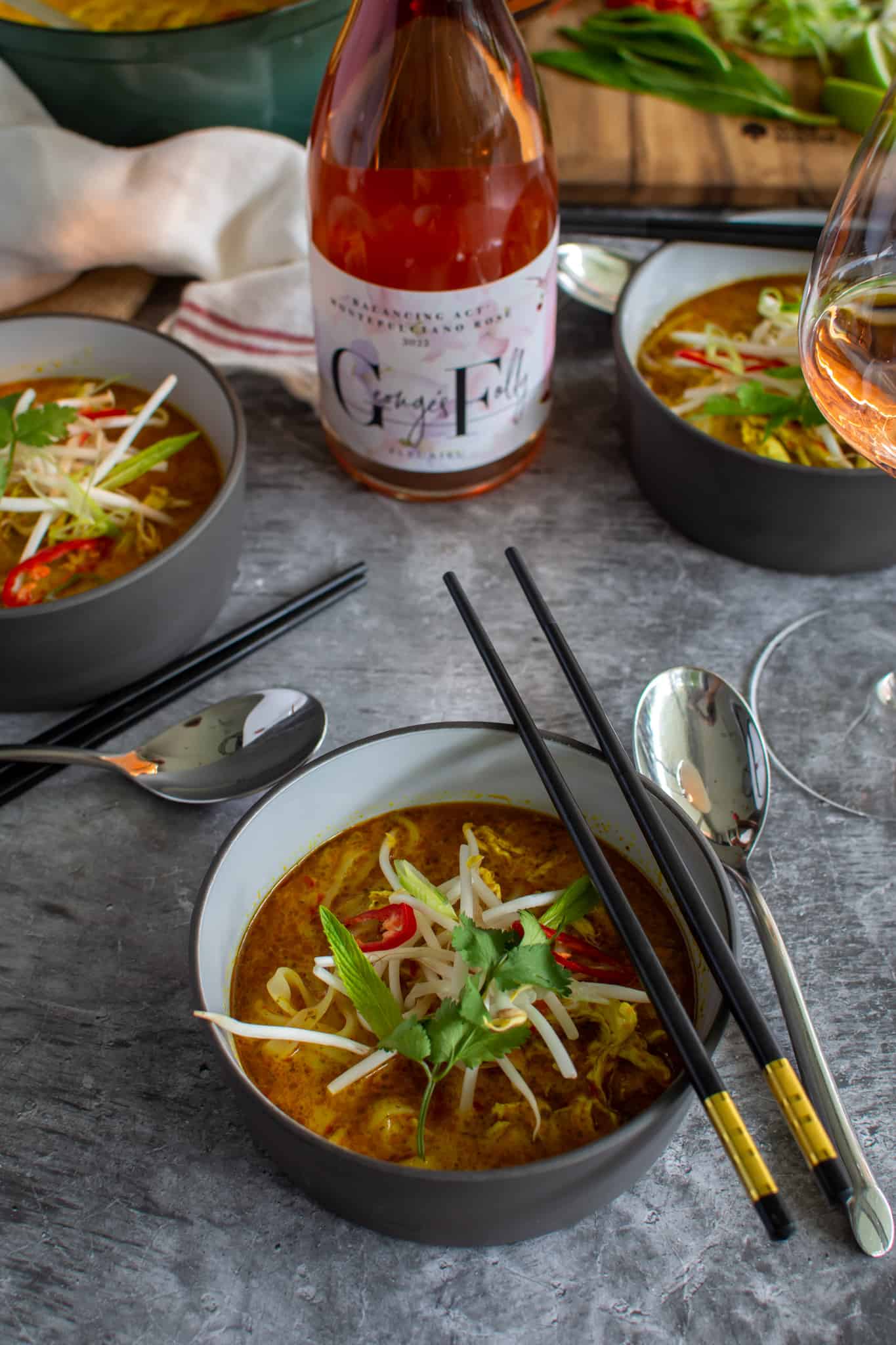 Bowl of chicken laksa soup with rose wine in the background