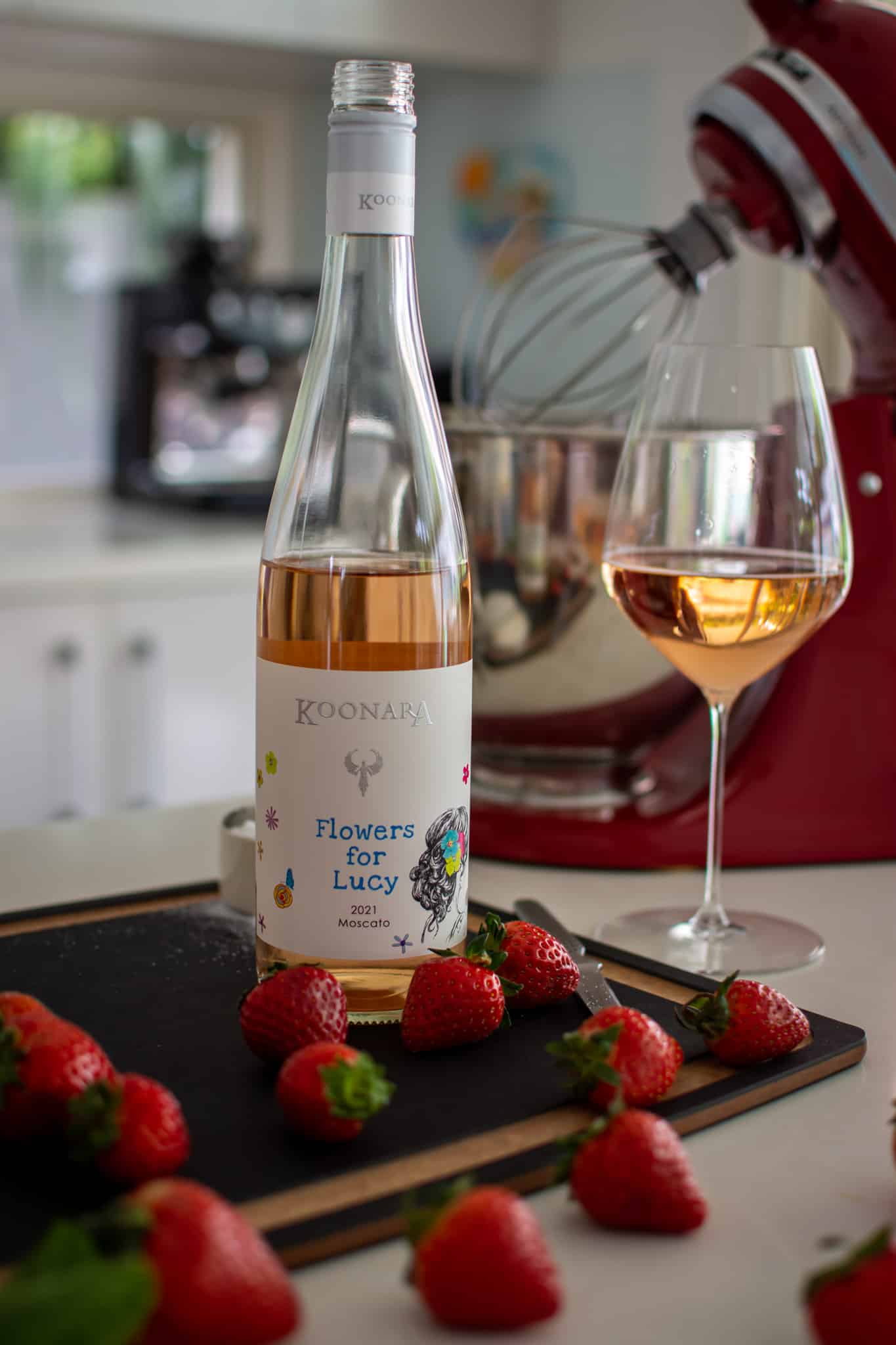 Koonara Moscato on chopping board in kitchen with loads of strawberries, wine glass and a kitchen aid mixer in the background