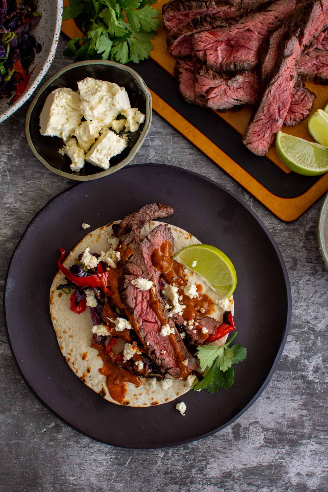 Birdseye view of grilled bavette steak tacos with sliced steak on chopping board and cabbage slaw in a bowl